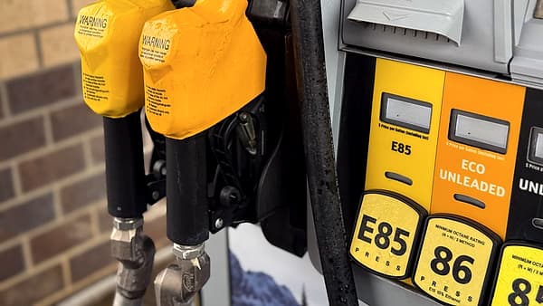 A fuel dispenser nozzle in a car filler neck with grade selection buttons and labels on the pump face