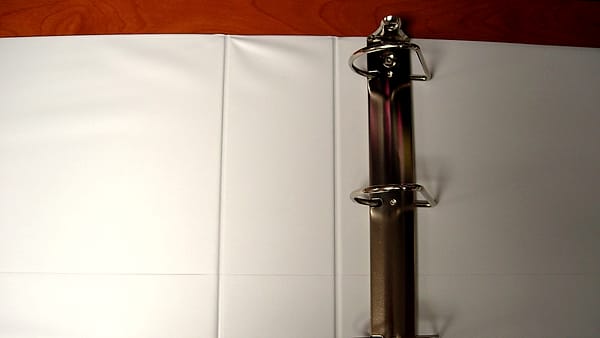 A row of labeled ring binders on a shelf with one pulled forward, its divider tabs visible above the pages