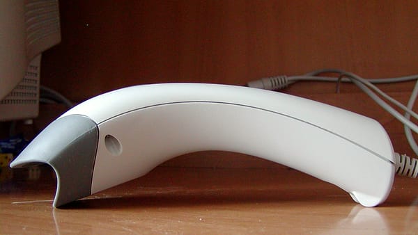 A handheld barcode scanner resting on a supermarket conveyor beside a small stack of grocery items