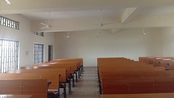 An examination room with rows of tables, mannequin heads on stands and numbered station cards laid out for candidates