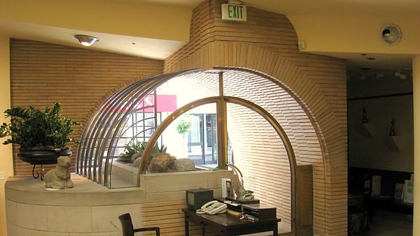 A small back-of-house room in a shop with a table, two chairs and a shelf of paperwork, door standing open to the aisle
