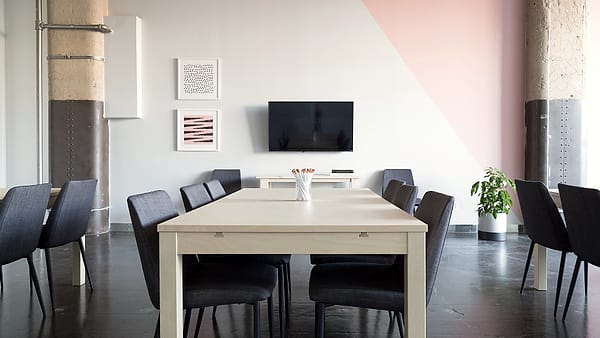 Two people seated at a small table in a plain office, one taking notes on a pad while the other speaks
