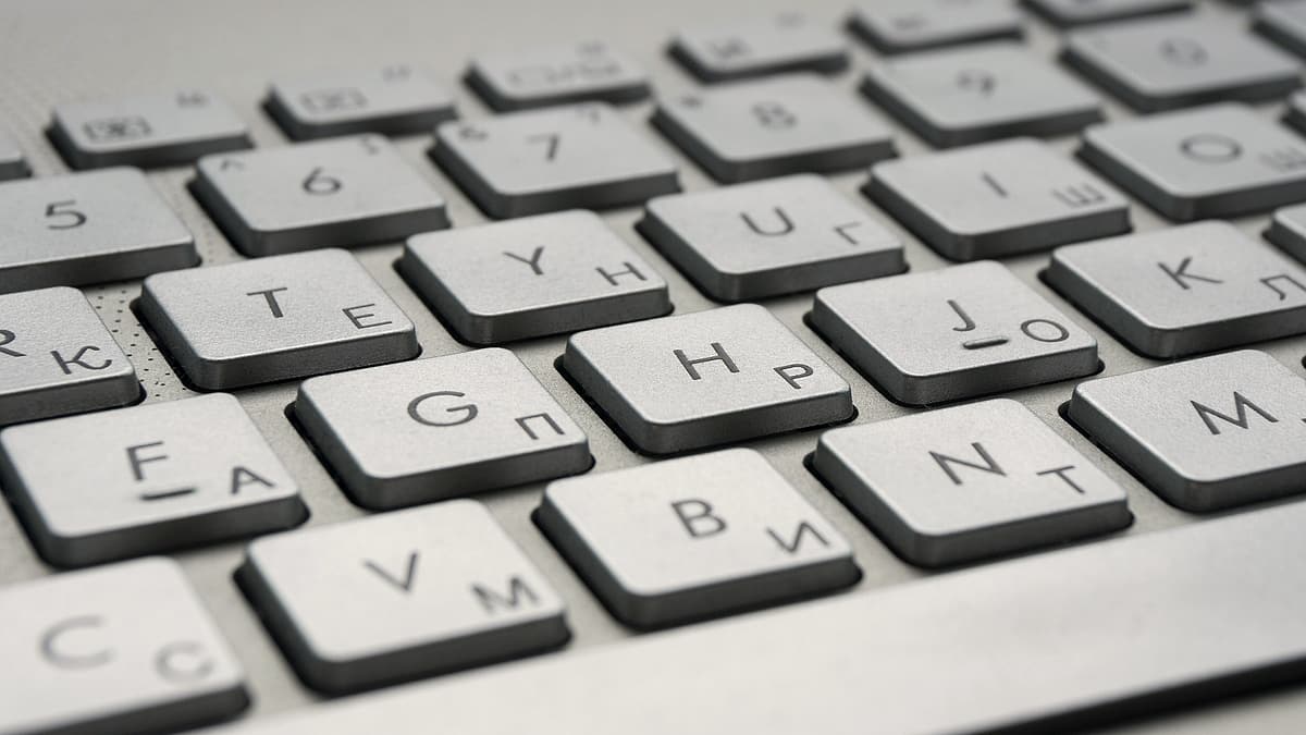 A person holding a phone in one hand and a printed statement in the other beside an open laptop on a desk